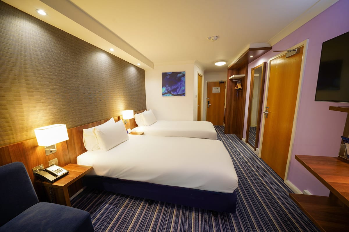 A hotel room with two beds, a desk with a lamp, a telephone, and a TV.
