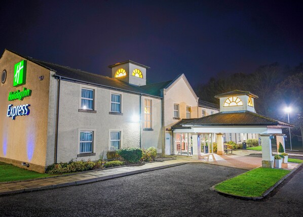 Edificio de Holiday Inn Express con una entrada bien iluminada y un área de estacionamiento.