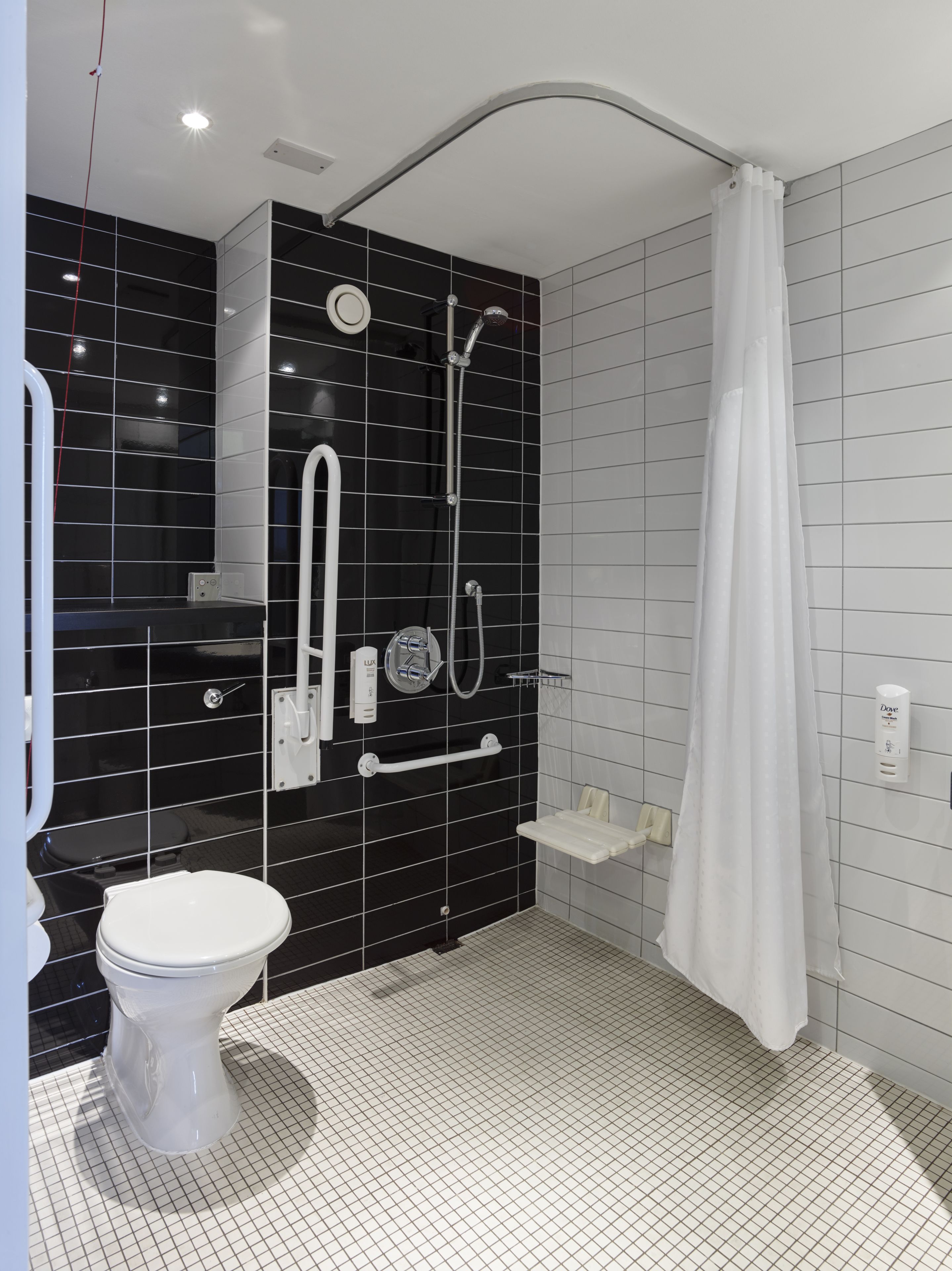 Une salle de bain moderne avec un carrelage noir et blanc, des toilettes blanches, un espace douche avec un rideau blanc et un sèche-mains.
