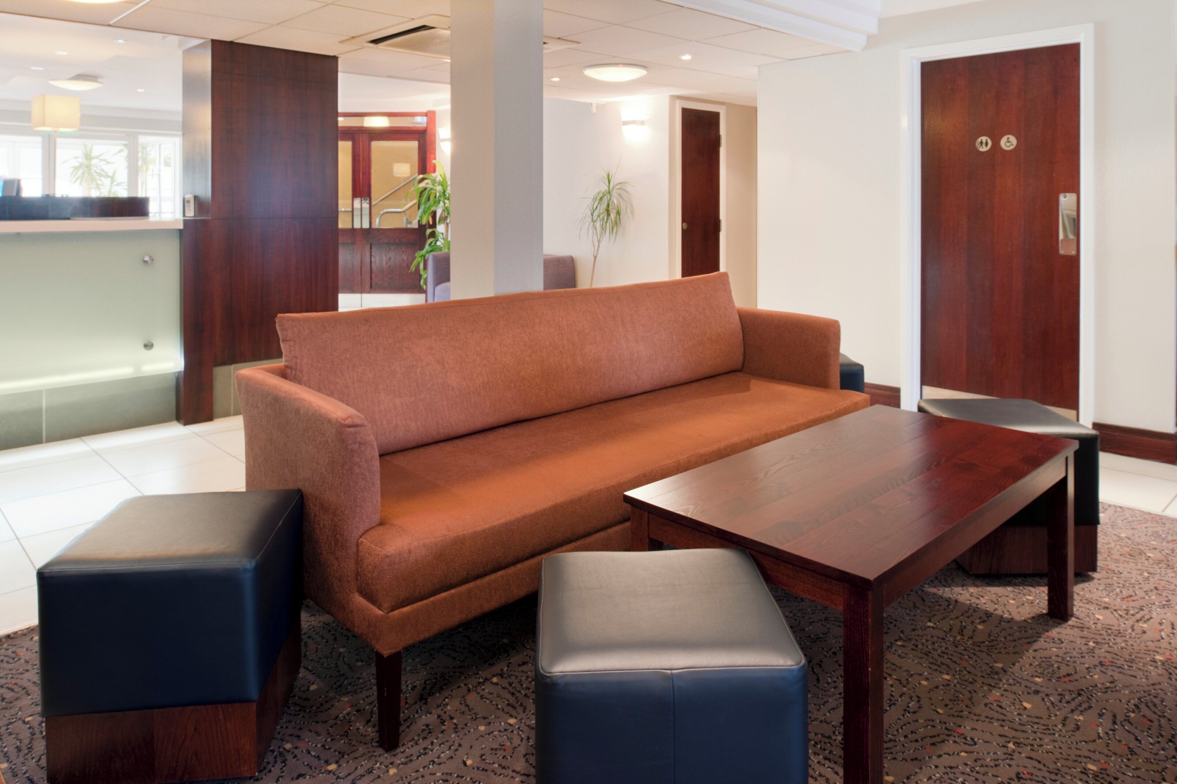 Un moderno vestíbulo de hotel con un sofá, un reposapiés y una mesa de centro de madera.