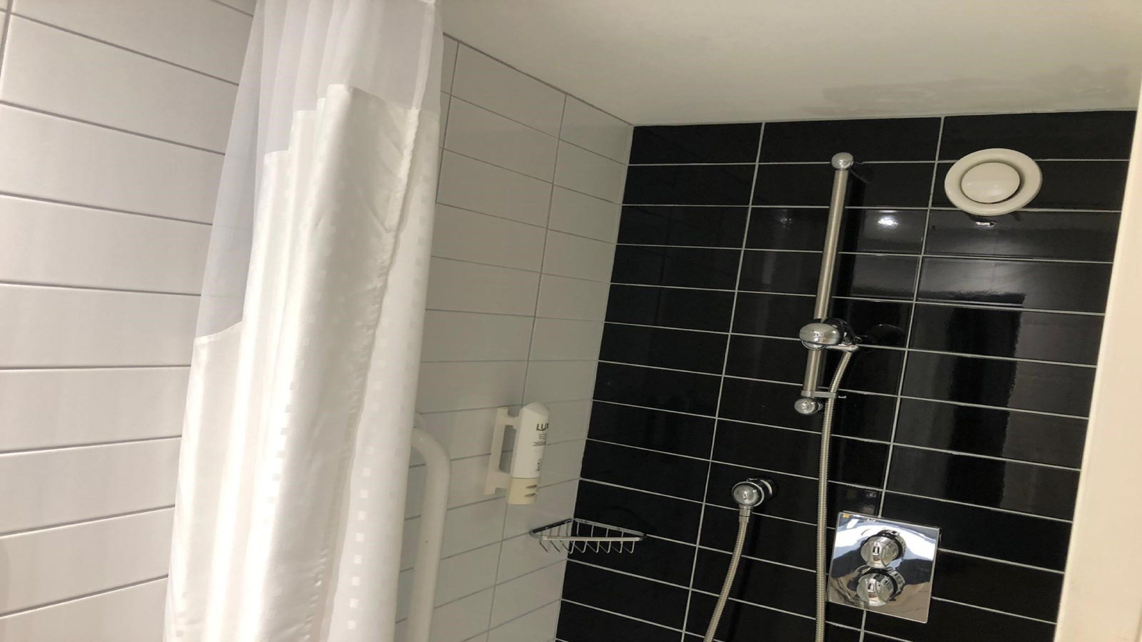 A bathroom with black tiled walls, a white shower curtain, and a handheld showerhead.