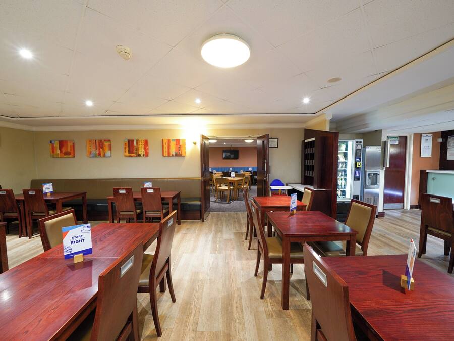 A dining area with wooden tables and chairs, a counter with a menu, and a television screen.