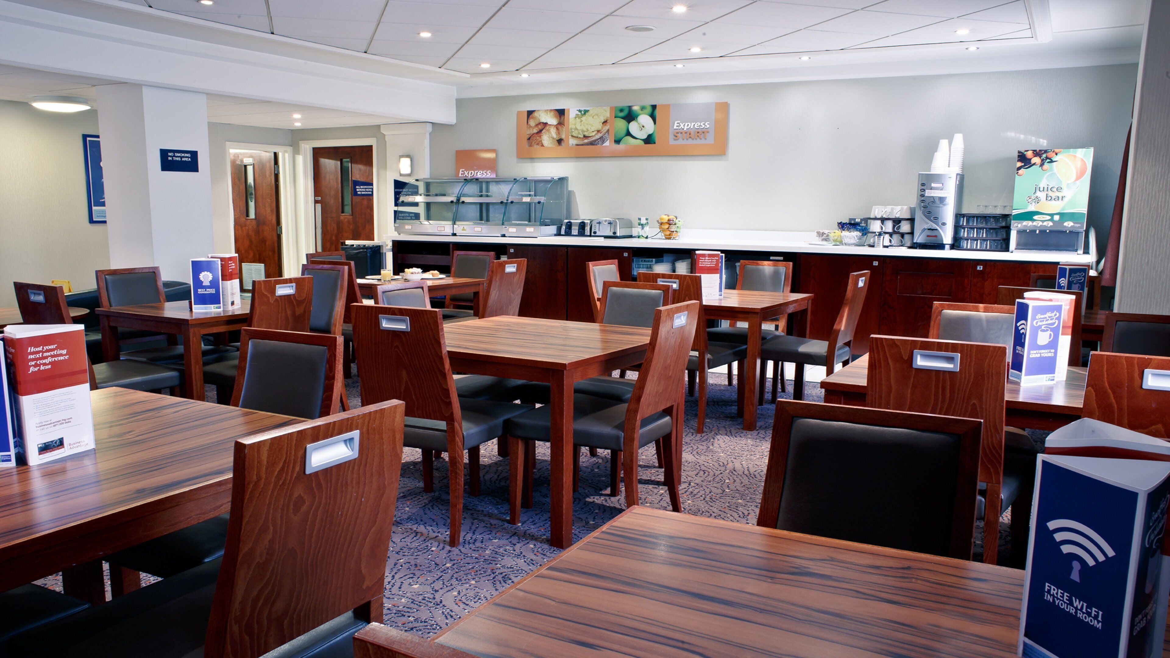 Comedor de hotel con varias mesas y sillas, un bar de zumos y una barra para buffet.
