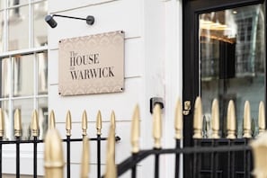 A sign reading "The HOUSE on WARWICK" mounted on a white wall with a black metal fence in front. - The Blair Victoria Hotel (London)