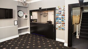 En hotellobby med en klocka, en kristallkrona, en receptionsdisk och en vägg full med vykort.