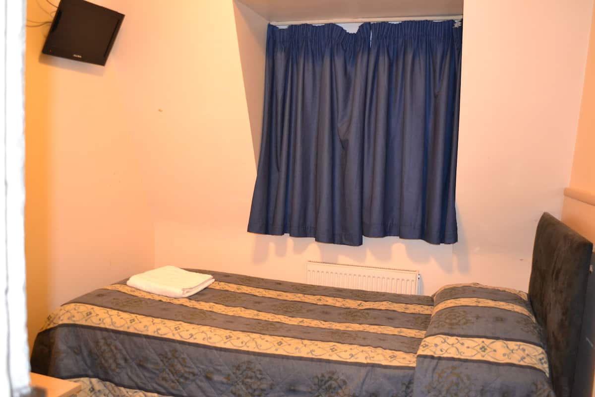A small bedroom with a bed, a radiator, a blue curtain, and a TV mounted on the wall.