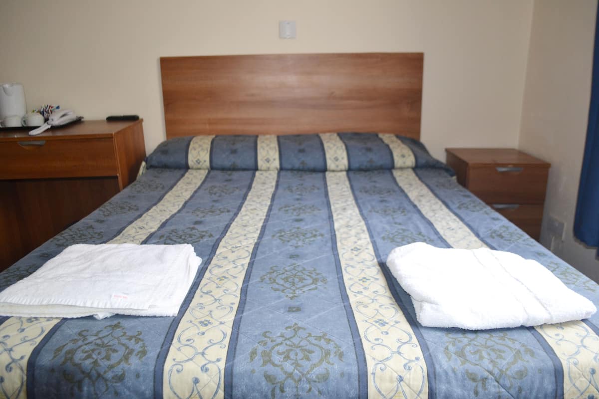 A neatly made bed with a patterned bedspread and two folded white towels.