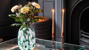 Et værelse med et glastæppe, hvor der står bøger, en vase med blomster og to tændte stearinlys.