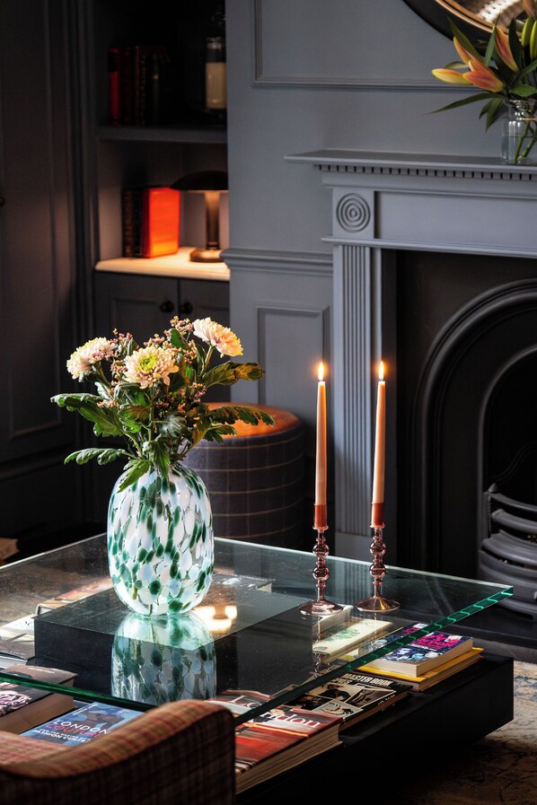 A room with a glass table displaying books, a vase with flowers, and two lit candles. - Tophams Hotel (London)