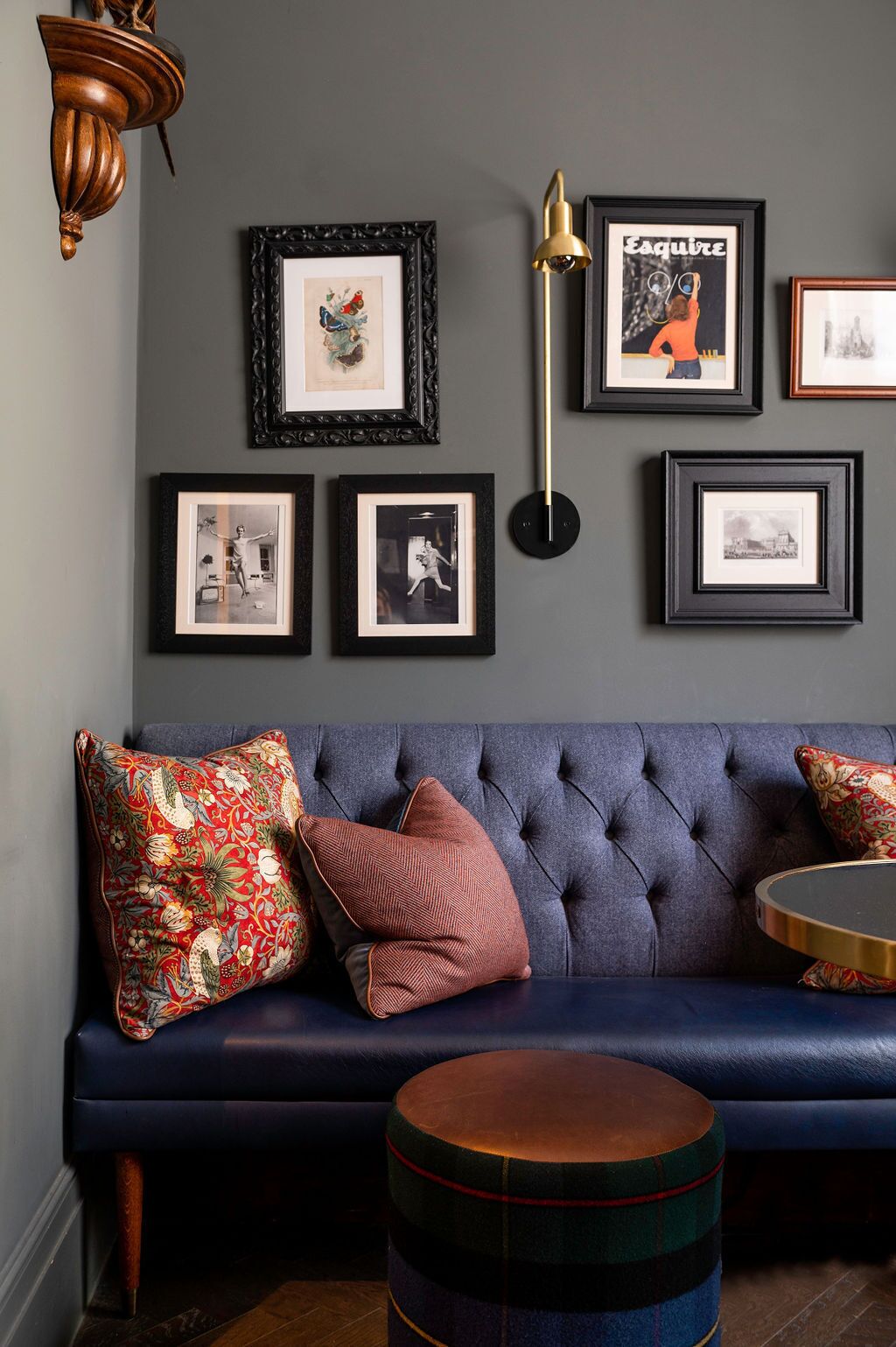 Una habitación con un sofá azul oscuro, varias fotografías enmarcadas en la pared, una mesa redonda de madera y una lámpara decorativa.