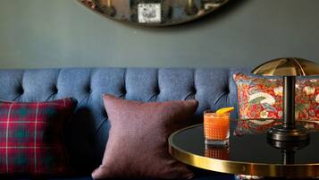 Ein blaues Sofa mit Kissen in Karomuster und einfarbigen Designs, ein runder Tisch mit einem Getränk und eine dekorative Lampe.