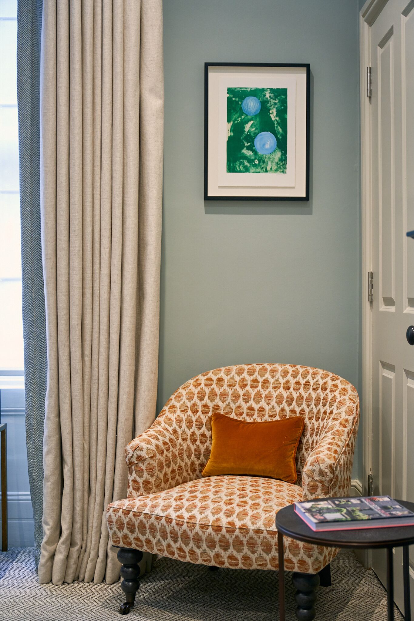 Una habitació amb un butac armchair estampat, una obra d'art emmarcada i una taula petita amb una revista.