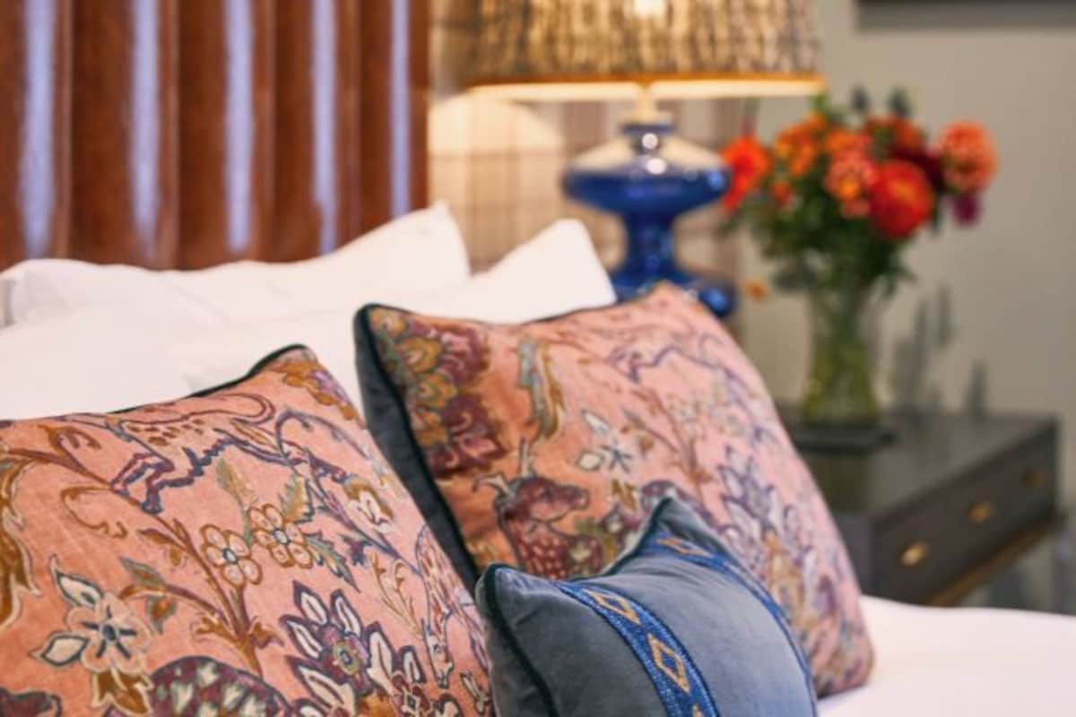 Ein Bett mit gemusterten Kissen und einer Blumenvase im Hintergrund.