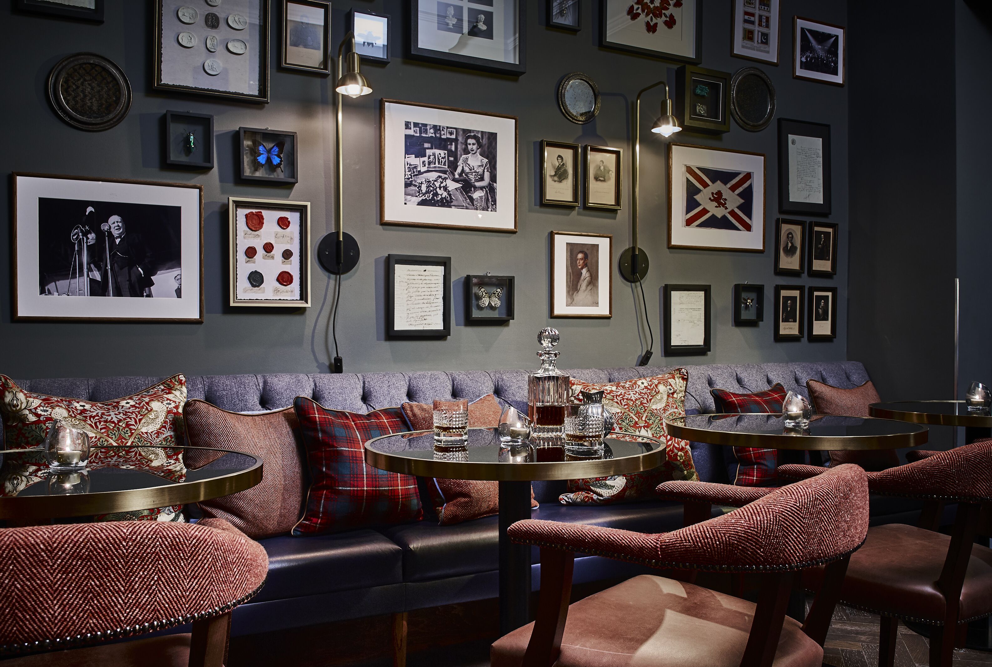A cozy lounge area with a sofa, two round tables, and a variety of framed pictures and coins on the wall.