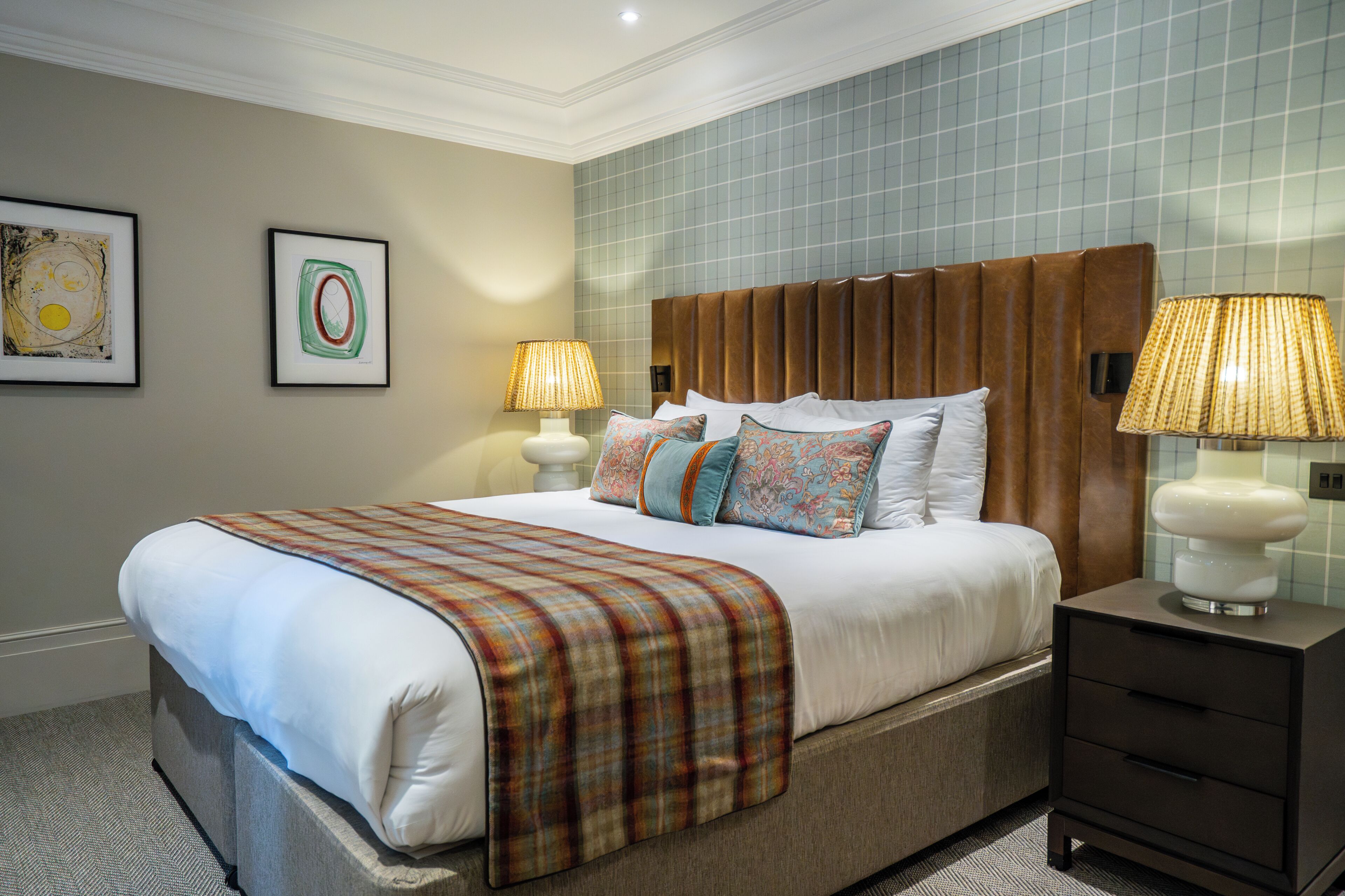 A neatly made bed with a plaid blanket, two bedside lamps, and a nightstand with a lamp.