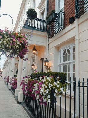 A row of numbered buildings with hanging flower baskets and black wrought iron railings. - Tophams Hotel (London)