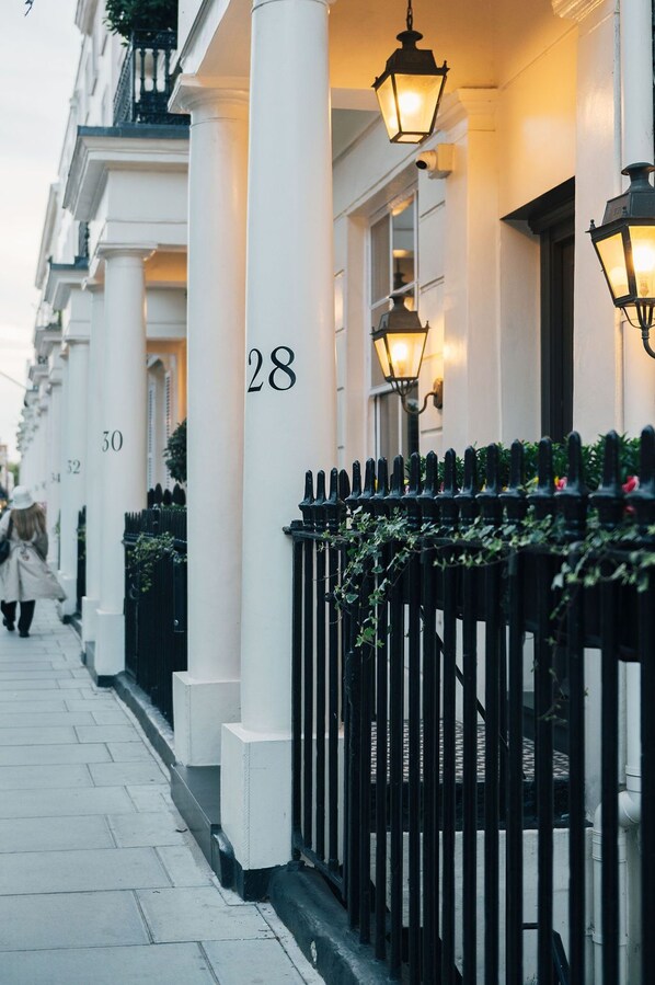 A row of numbered buildings with a black iron fence and greenery in front. - Tophams Hotel (London)