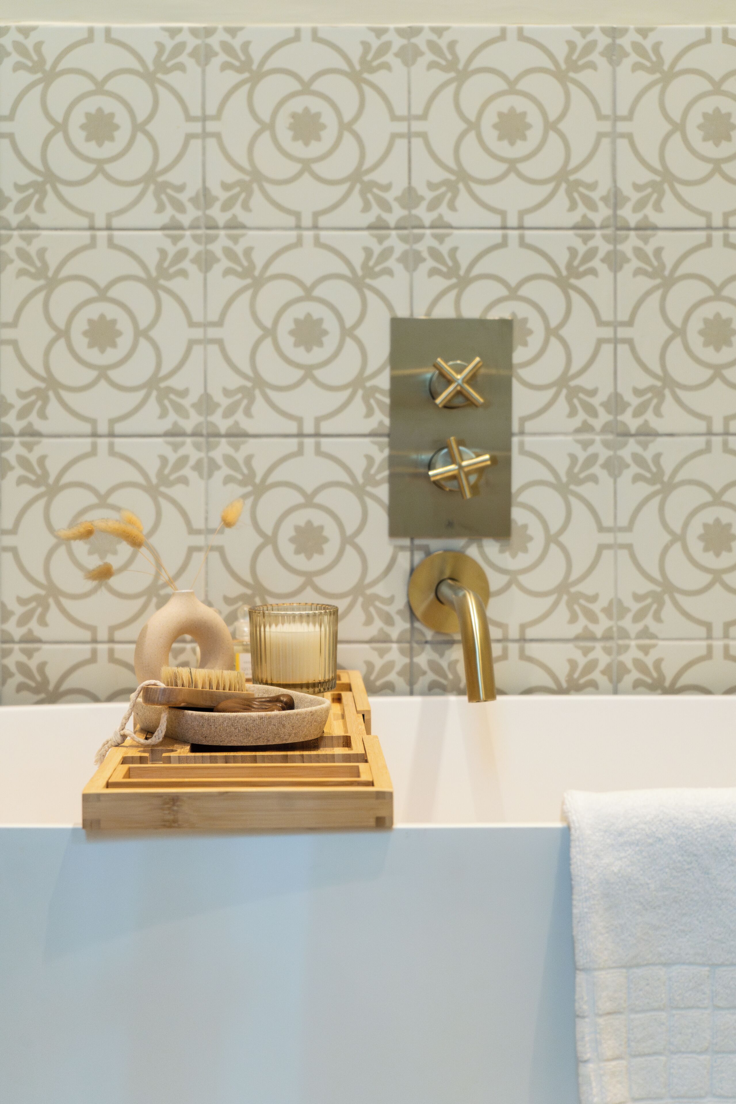 Un baño con una bañera blanca, una bandeja de madera con artículos de aseo, un grifo dorado y un papel tapiz estampado.