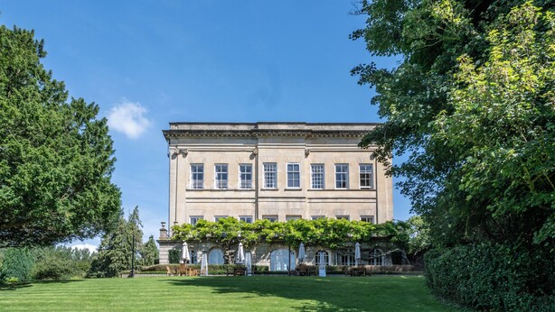 A large, historic building with a symmetrical facade, multiple windows, and a well-maintained lawn in front.