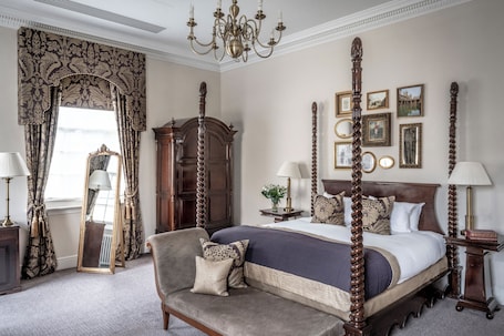 A classic four-poster bed with a dark wooden frame, a large mirror, and a chandelier.. Bailbrook House