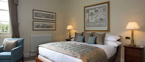 A bedroom with a large bed, two bedside tables, a chair, and framed artwork on the wall.