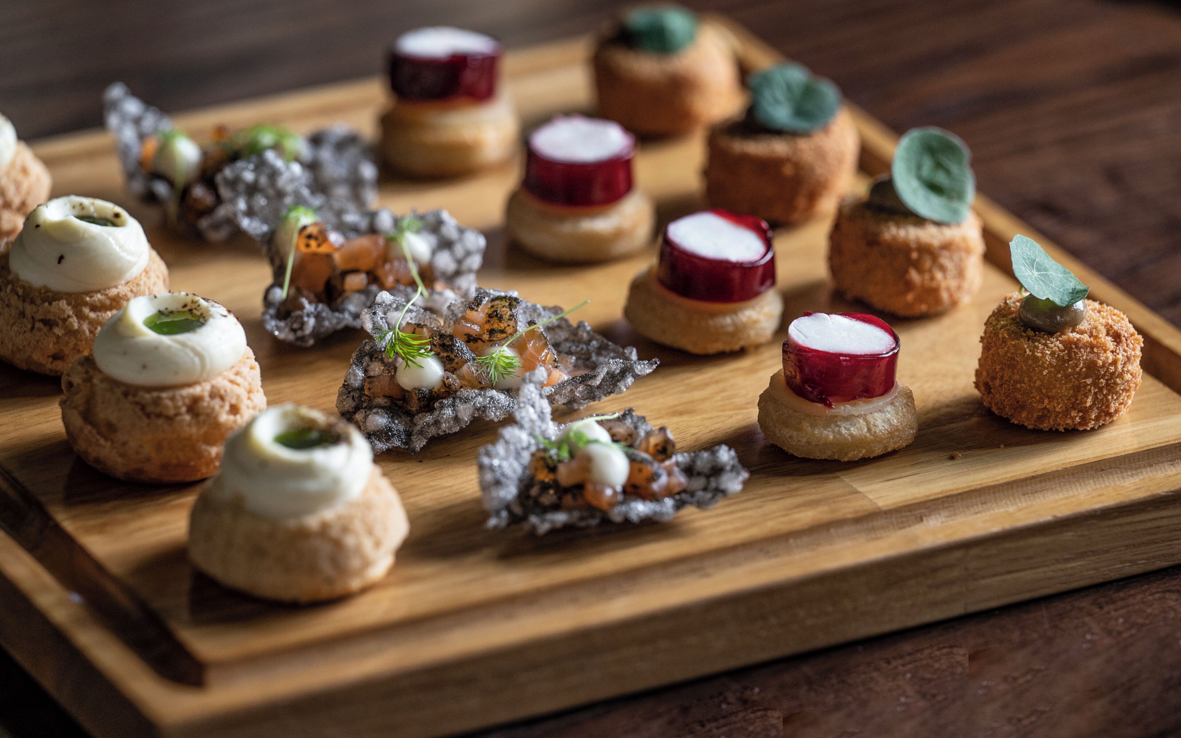 Verschiedene kleine, runde Desserts auf einer Holzplatte.