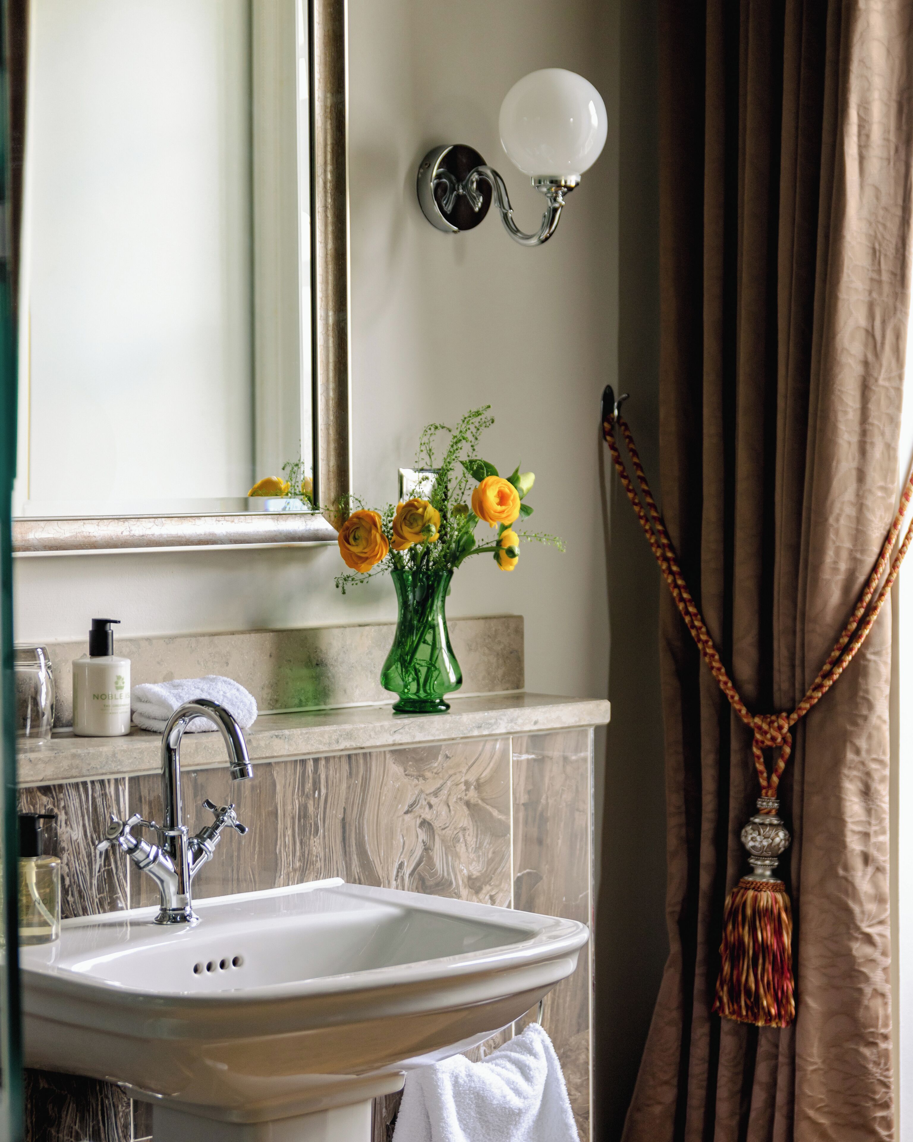 Un bagno con lavandino, specchio, vaso con fiori e asciugamano.
