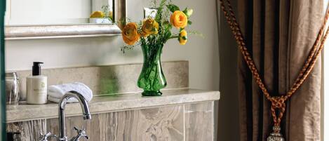 A bathroom with a sink, mirror, vase with flowers, and a towel.