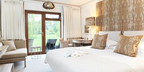 A hotel room with a large bed, a desk, a chair, and a view of a garden through the door.