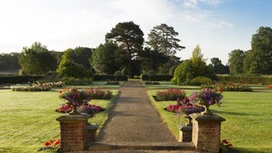 A formal garden with a gravel path leading to a central point, surrounded by neatly trimmed hedges and flower beds. - Champneys Tring (Tring)