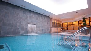 An indoor swimming pool with a waterfall feature, surrounded by stone walls and modern lighting. - Champneys Tring (Tring)