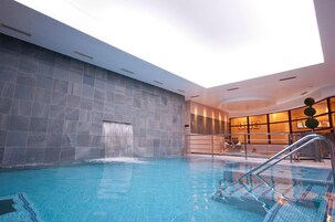 Piscina interior com cachoeira, rodeada por paredes de pedra e iluminação moderna.
