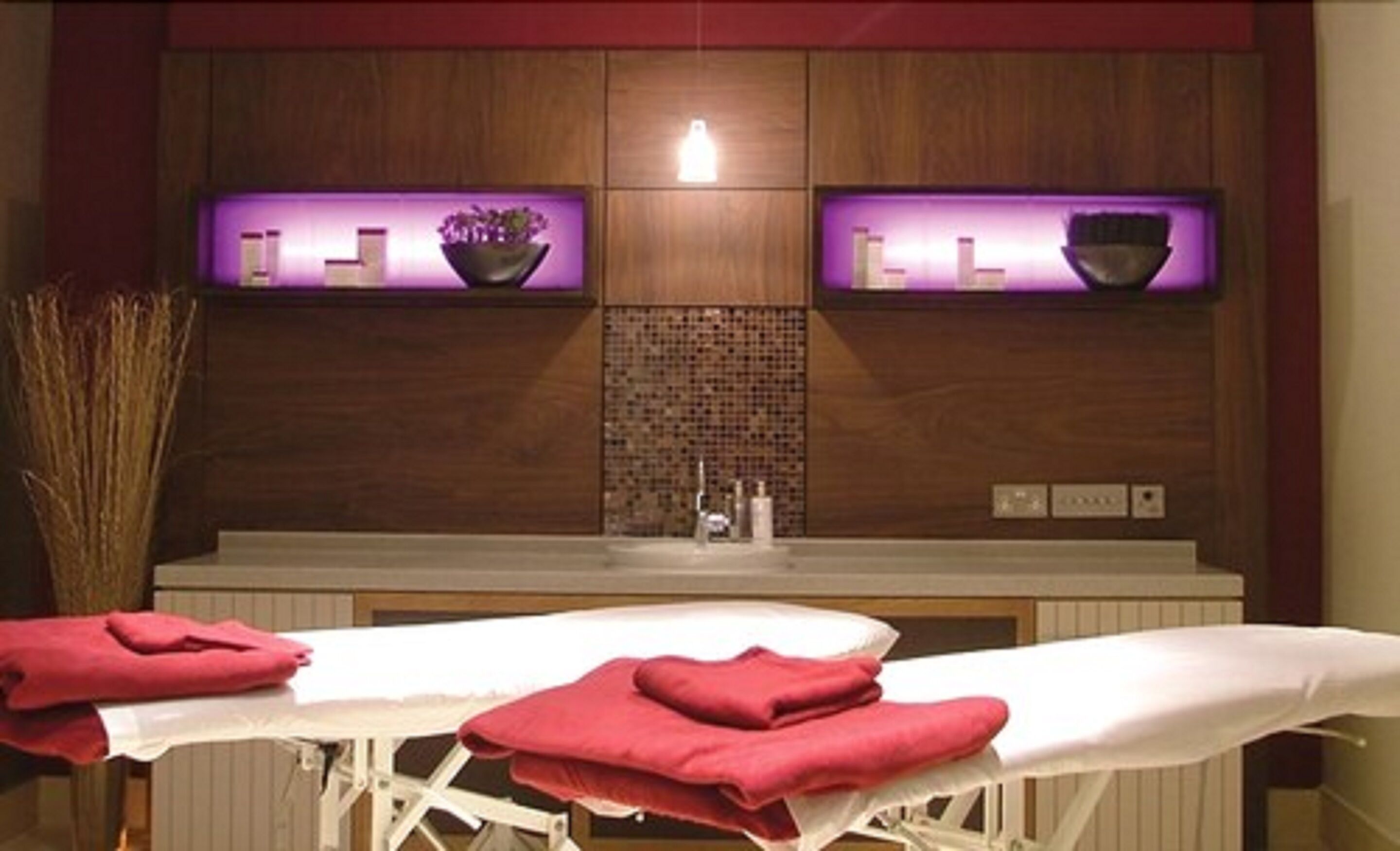 A spa room with a massage table, red towels, a sink, and a mirror.