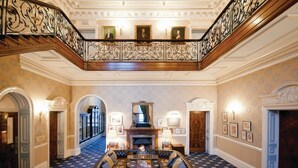 A grand lobby with a high ceiling, ornate iron railing, a fireplace, and a patterned carpet. - Champneys Tring (Tring)