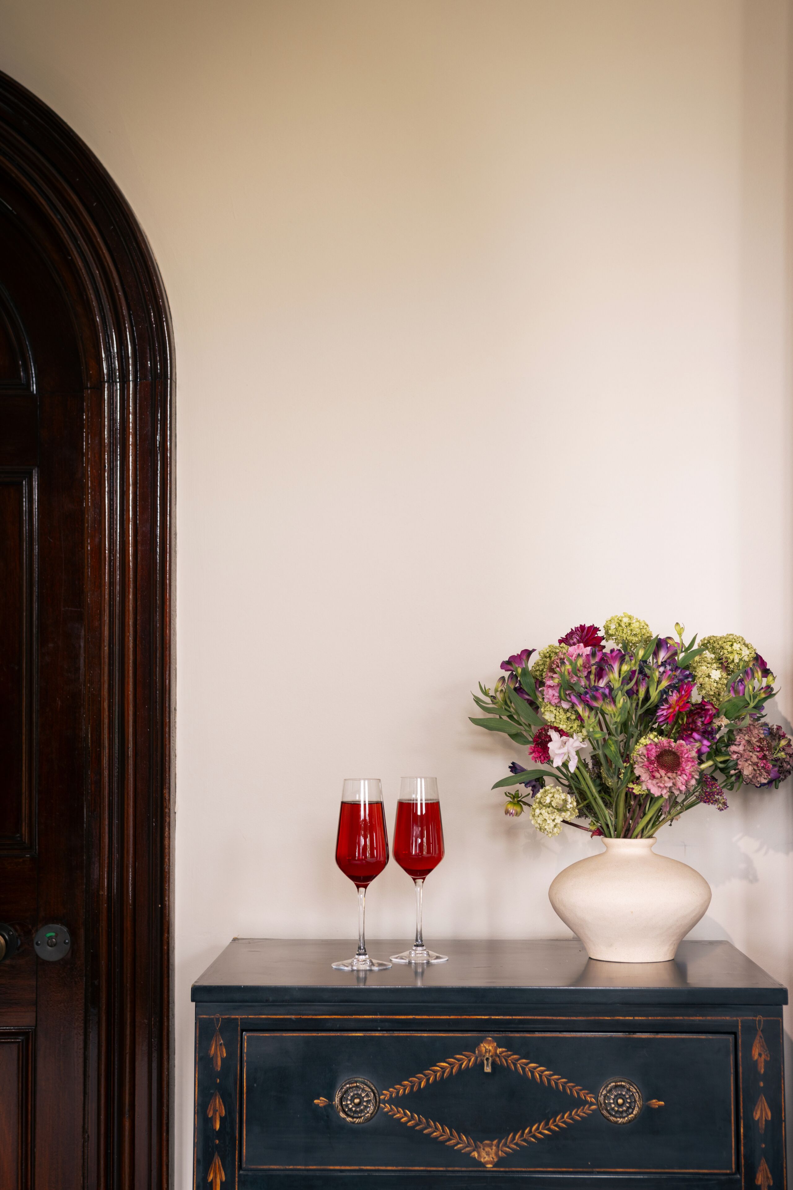 A dark wooden cabinet with two wine glasses and a vase of flowers.