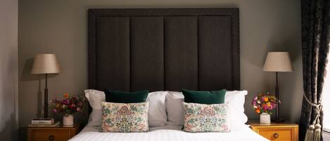 A neatly made bed with striped bedding, two nightstands with lamps and flower vases, and a dark headboard.