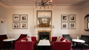 A room with a fireplace, red sofas, a chandelier, and framed pictures on the walls. - Rookery Hall Hotel (Nantwich)