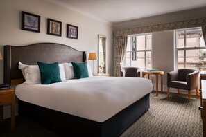 Habitación de hotel con una cama grande, un escritorio, una silla, una mesita y una ventana con cortinas.