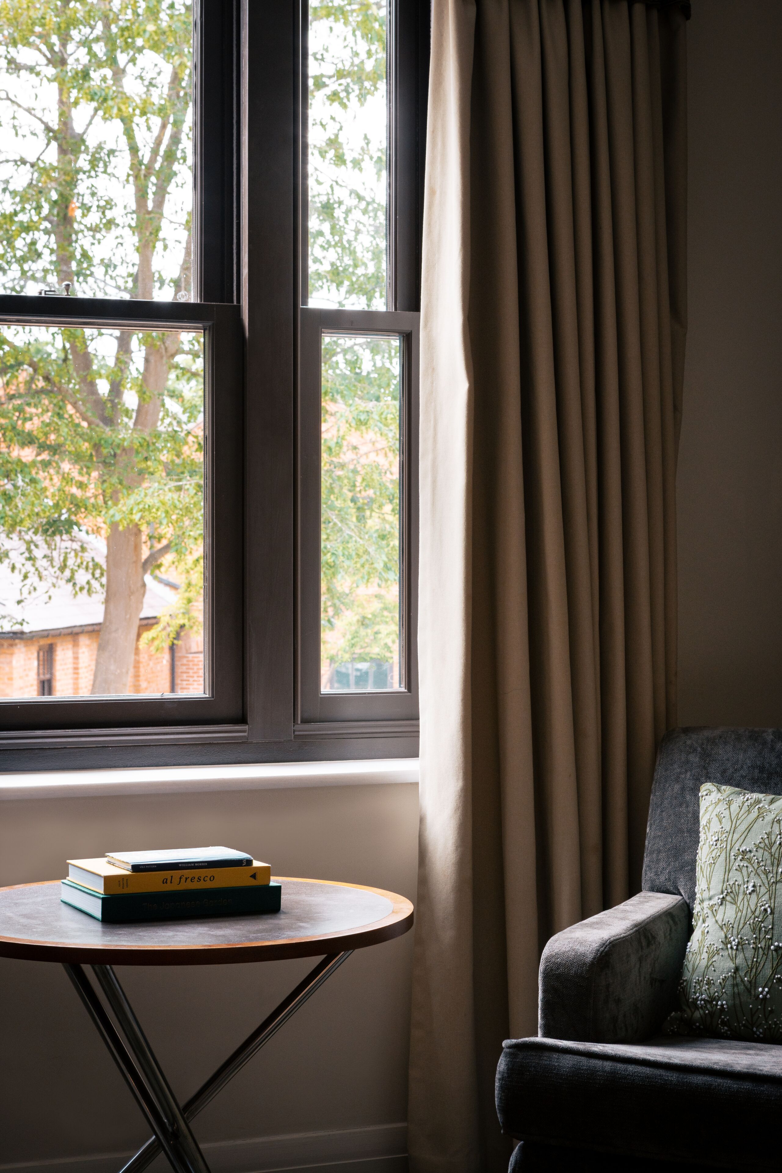 A room with a window, a chair, a small table with books, and a curtain.