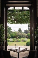 Uma área de jantar com mesa posta para quatro pessoas, com vista para um jardim com uma fonte e vegetação exuberante.