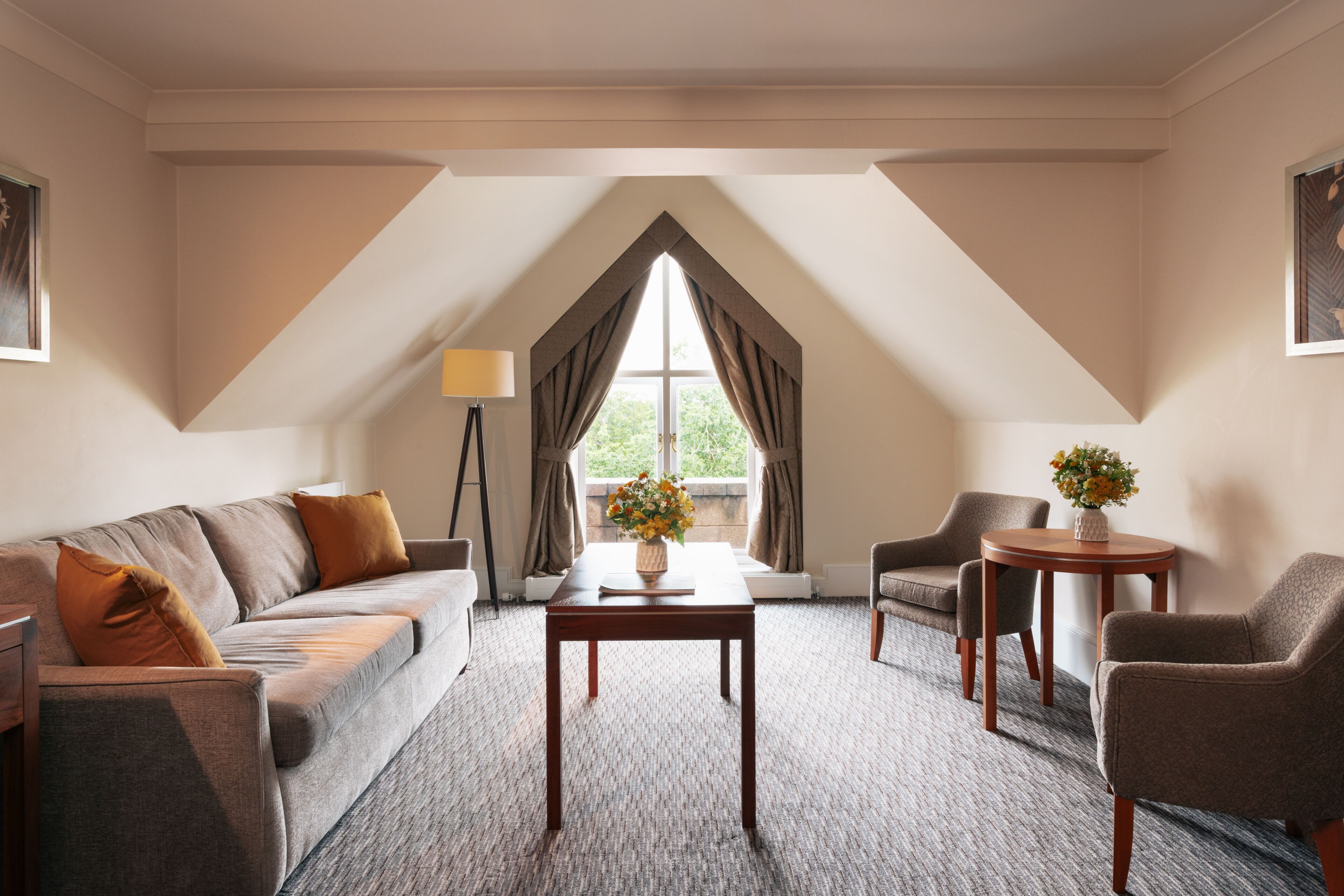 Habitación de hotel con sofá, sillones, una mesita y una ventana con cortinas.