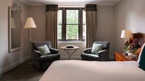 A hotel room with a bed, two armchairs, a small table, a mirror, and a window with curtains. - Rookery Hall Hotel (Nantwich)