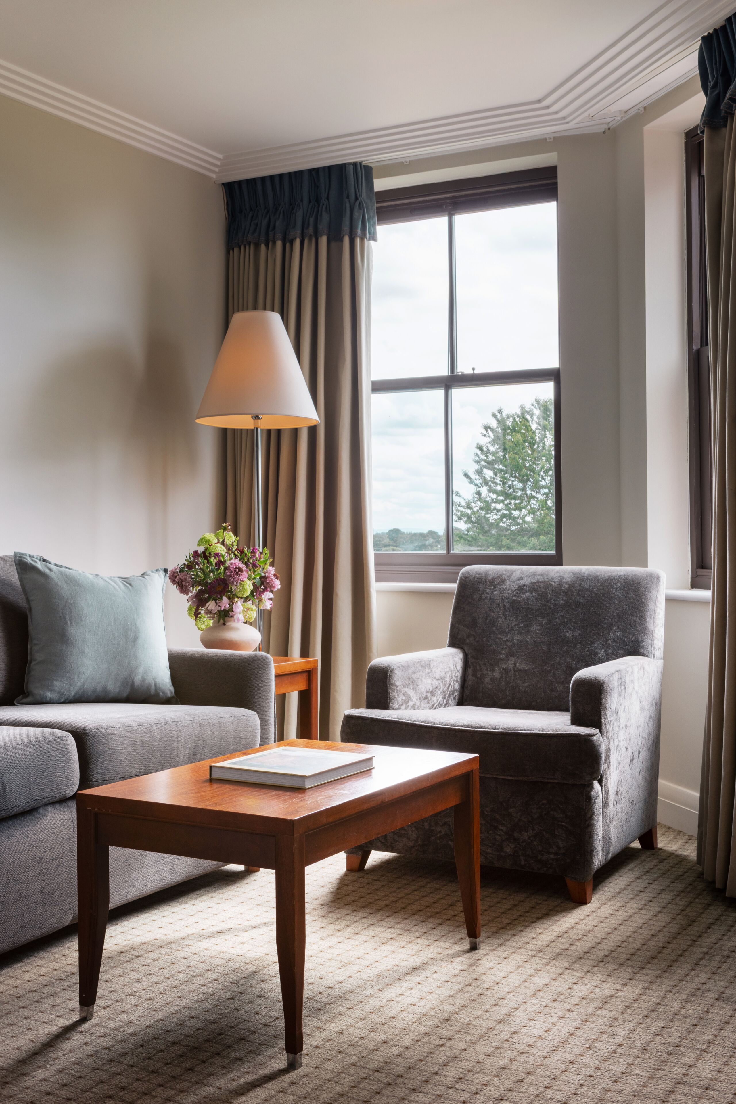 Un salon comprenant un canapé, un fauteuil et une table basse, une lampe et une fenêtre avec des rideaux.