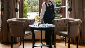 A room with a large window, two chairs, a table, and a person serving. - Rookery Hall Hotel (Nantwich)