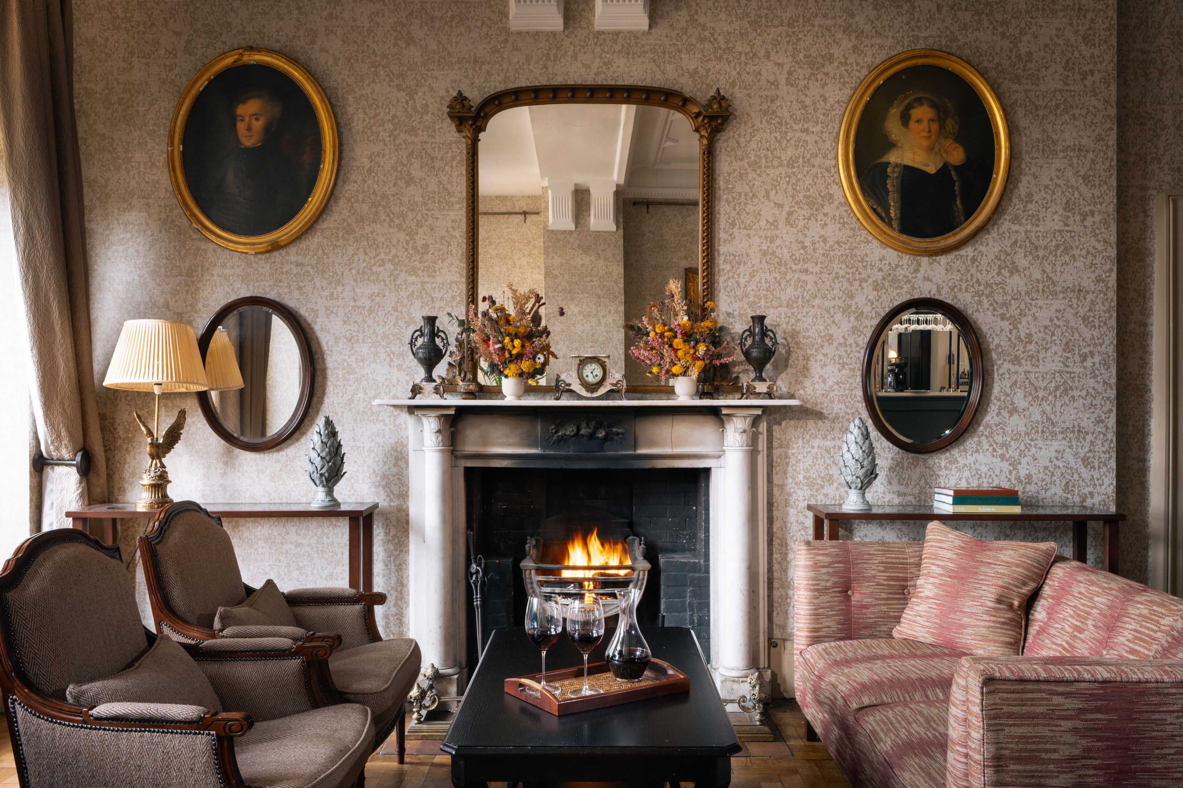A traditional room with a fireplace, two armchairs, a sofa, and a table with a tray of glasses.