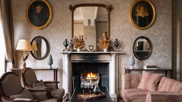 A traditional room with a fireplace, two armchairs, a sofa, and a table with a tray of glasses.