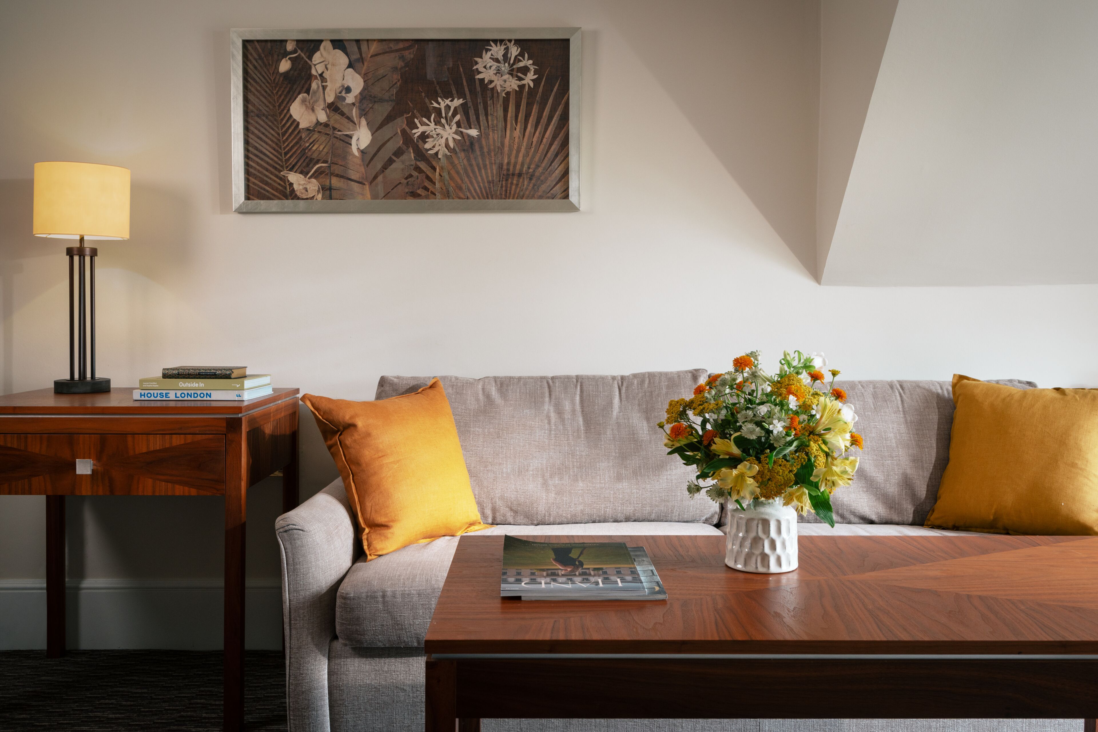 Une pièce comprenant un canapé, une table basse, une lampe, un tableau encadré et un vase avec des fleurs.