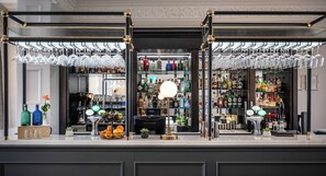 Zona de bar con mostrador, estantes llenos de botellas de licores y copas de vino colgantes.