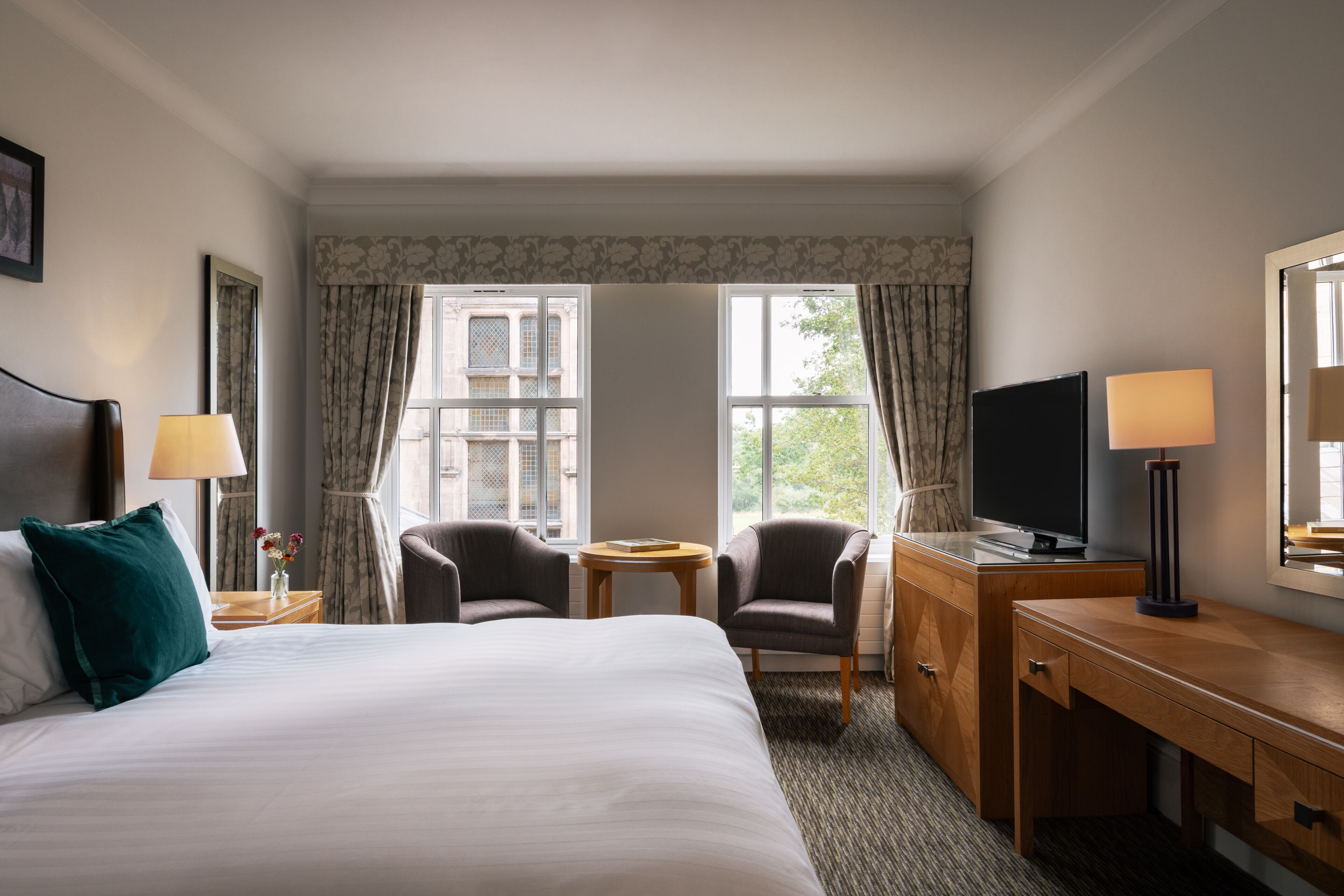 A hotel room with a bed, two armchairs, a desk with a TV, and a window with curtains.