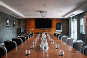 A conference room with a long table, chairs, a television screen, and a Harrogate branded bottle. - Rookery Hall Hotel (Nantwich)